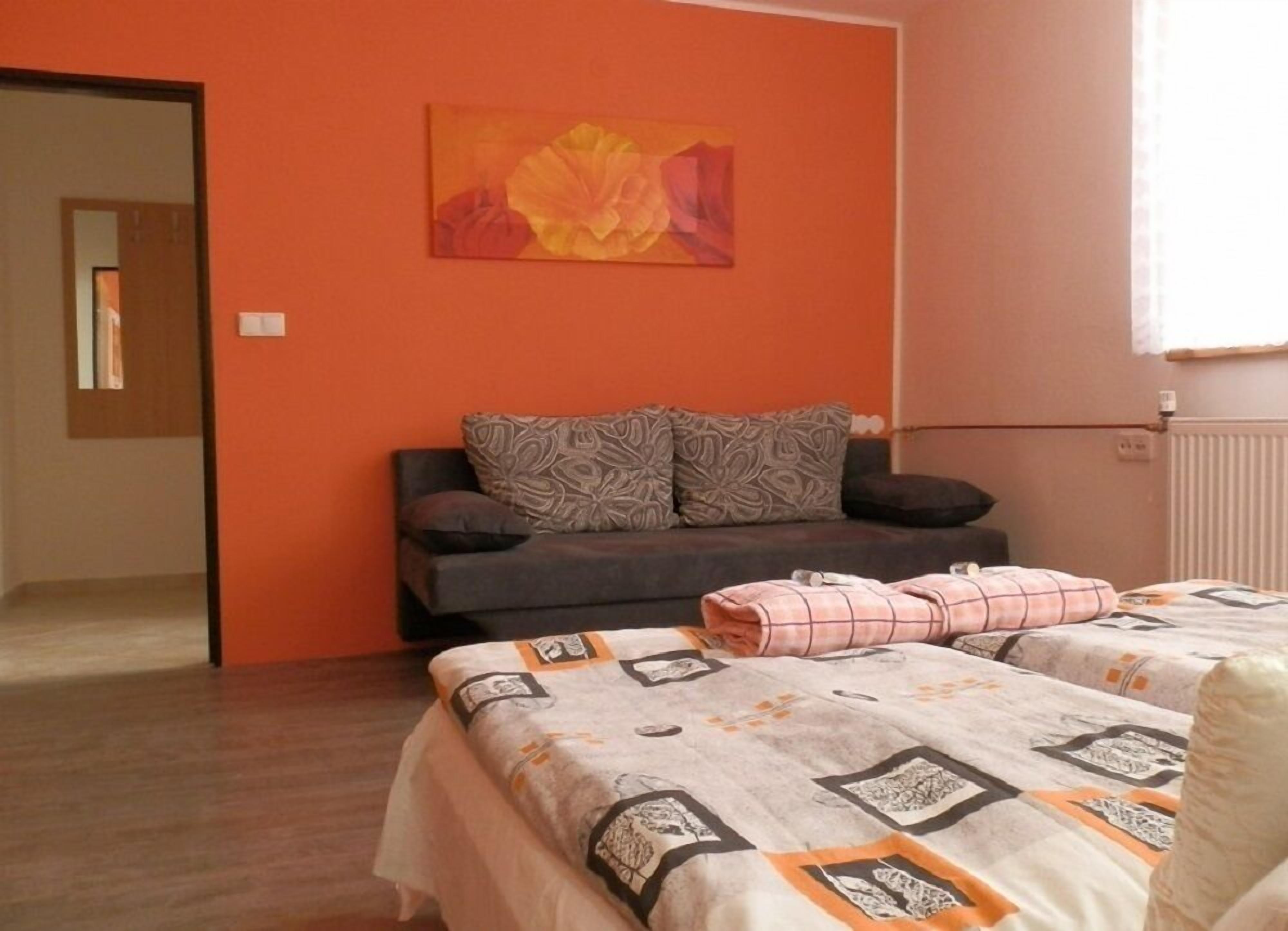 A bedroom with a sofa bed, a patterned bedspread, and a floral painting on the wall.