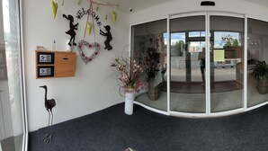 A hotel reception area with a glass door, a wooden desk, a trash bin, and a wall-mounted information board. - Hotel Gól Prostějov (Prostejov)