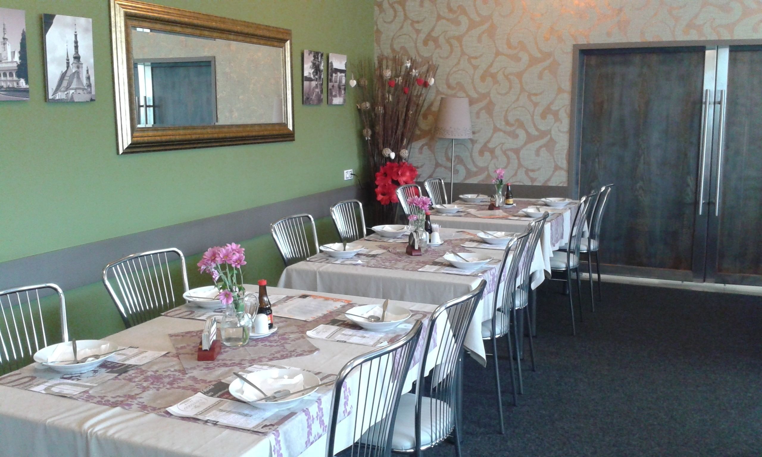 Un espace repas avec une longue table dressée pour accueillir plusieurs convives, des chaises, un miroir et des éléments de décoration murale.