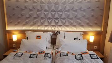 Habitación de hotel con cabecera de diseño geométrico, dos camas con ropa de cama estampada y lámparas de noche.