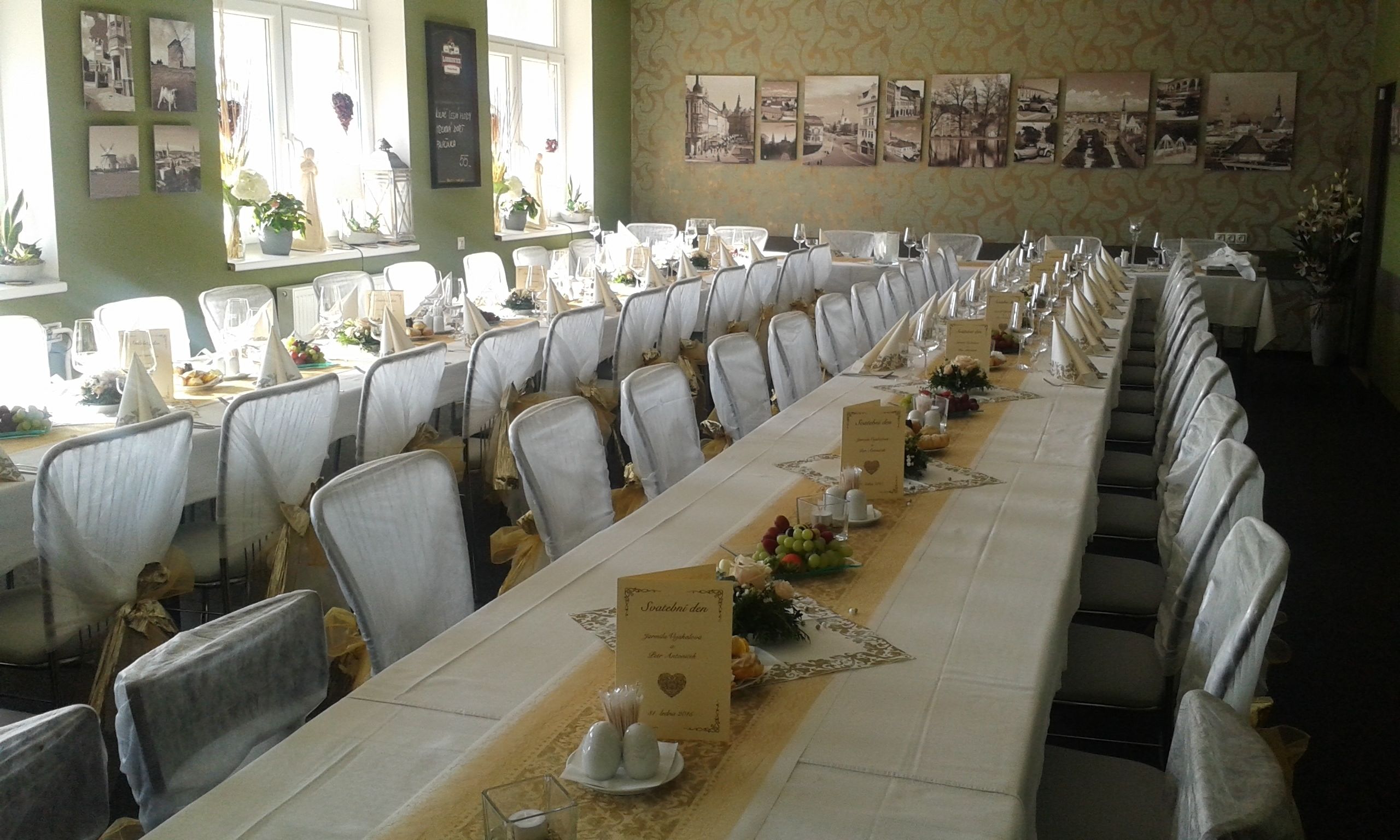 A long dining table set with chairs, menus, and floral centerpieces in a room with patterned wallpaper and framed pictures on the walls.