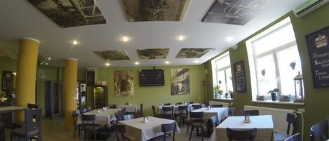 Un restaurante con varias mesas y sillas, una pared verde y decoración en el techo.
