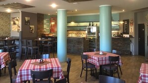 A restaurant with tables covered in red and white checkered tablecloths, wooden chairs, and a bar area with a stone counter. - Hotel Gól Prostějov (Prostejov)