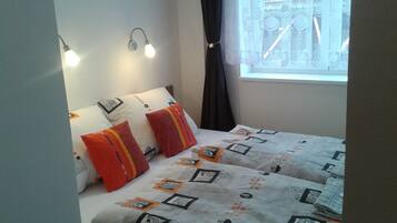 Un lit bien fait, avec une literie à motifs, un luminaire fixé au mur et une fenêtre agrémentée de rideaux décoratifs.