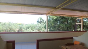 A covered balcony with a wooden table and chairs, a view of greenery, and a ladder leaning against the wall. - Residence Giardino (Vieste)