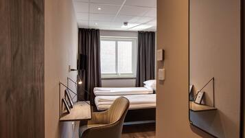 A hotel room with a bed, a desk, a chair, a TV, and a window with curtains.