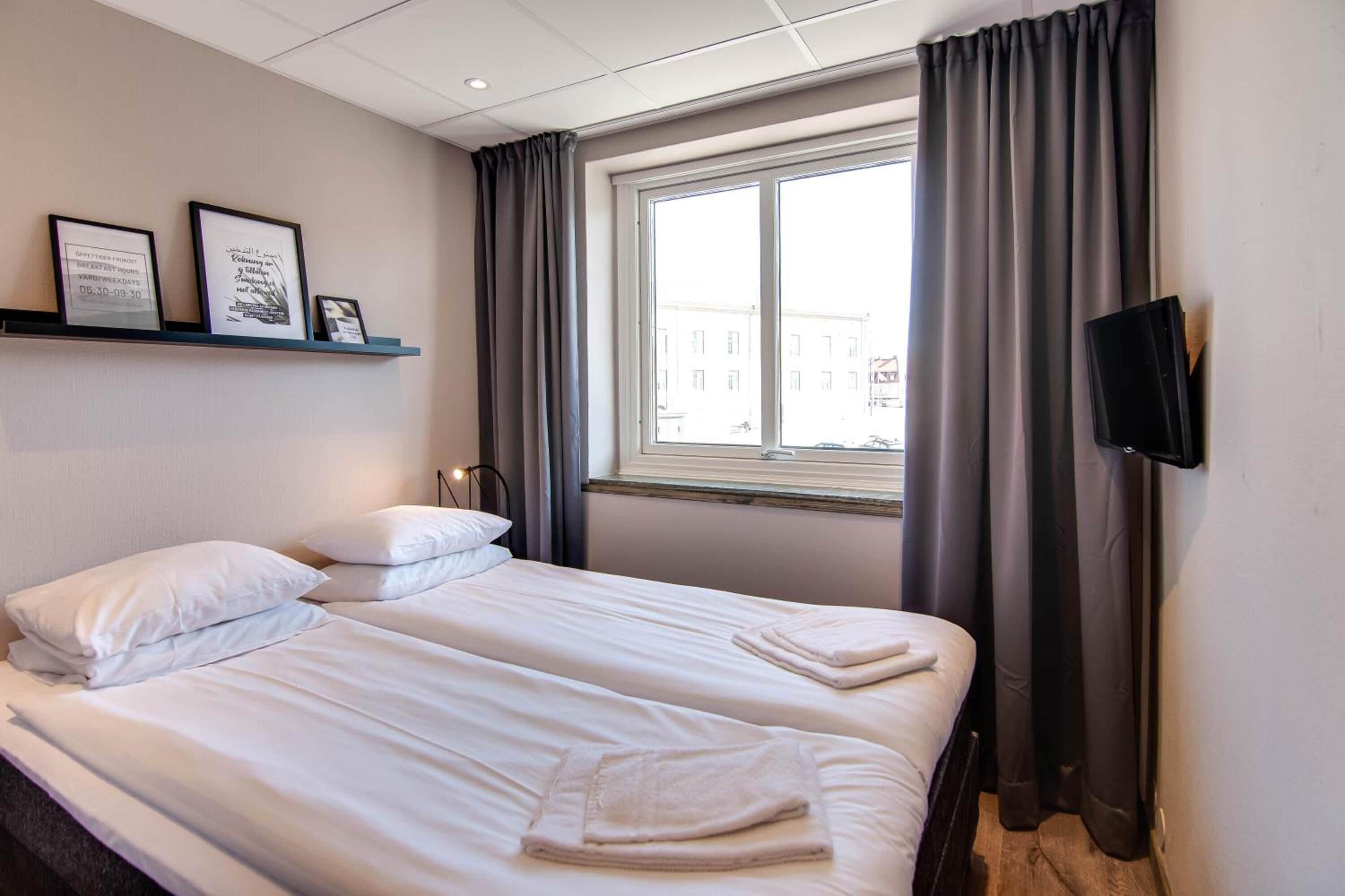 Ein Hotelzimmer mit zwei Betten, einem an der Wand befestigten Fernseher und einem Fenster mit Vorhängen.