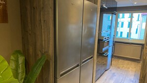 A modern kitchen with a stainless steel refrigerator, wooden cabinets, and a view of the city through a large window. - Karlskrona H&H (Karlskrona)