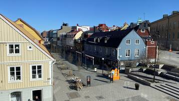A cobblestone square with historic buildings, a tram stop, and a clear blue sky.