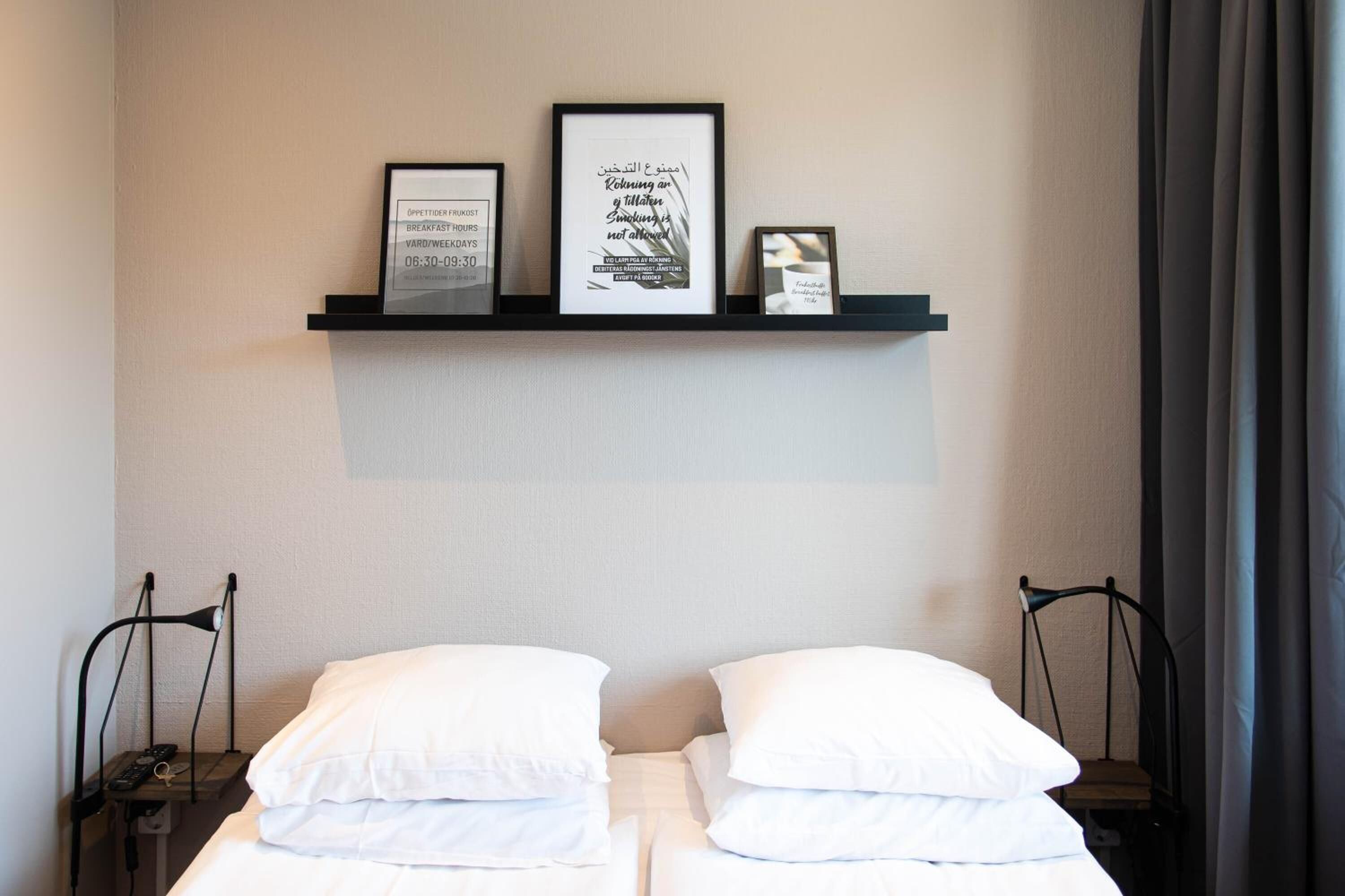 A hotel room with a bed, two bedside tables, a shelf with framed pictures, and a chair.