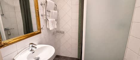 Un baño con lavamanos blanco, un espejo con marco dorado, toallero y cabina de ducha.