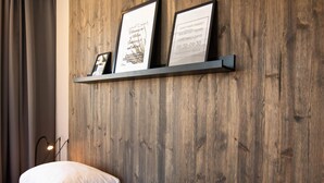 A hotel room with a wooden wall, a shelf with framed pictures, a bed with white bedding, and a bedside lamp. - Karlskrona H&H (Karlskrona)