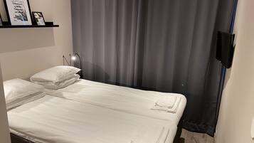 Ett hotellrum med en säng, kuddar, ett sängbord, en lampa och en gardin.
