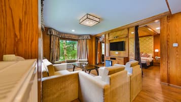 A hotel room with a wooden interior, a large window with curtains, a sofa set, a television, and a bed.