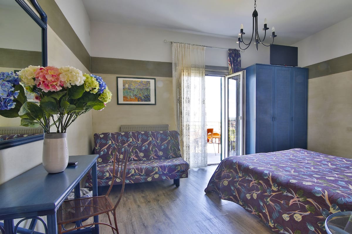 A bedroom with two beds, a chair, a table, a vase with flowers, a painting, and a wardrobe.