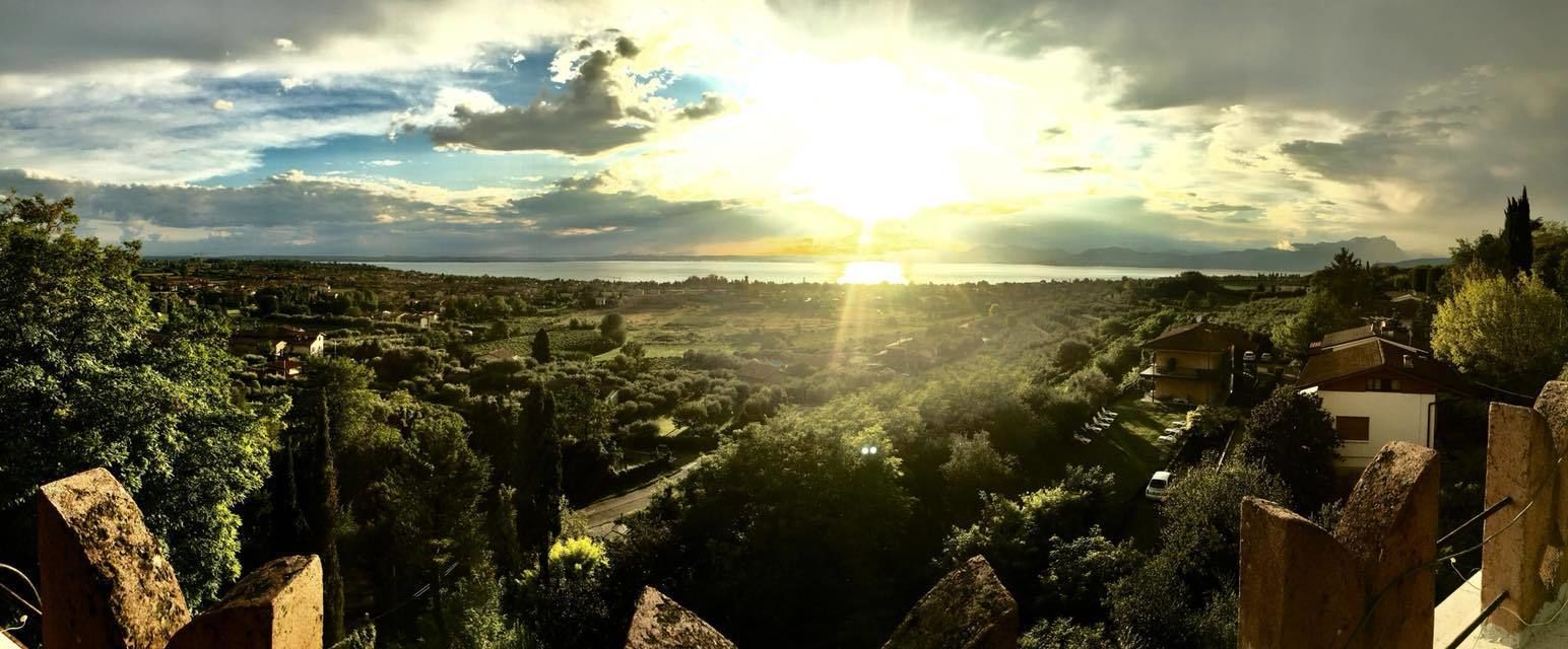 A panoramic view of a coastal town with a prominent sun setting over the horizon, surrounded by lush greenery and traditional architecture.