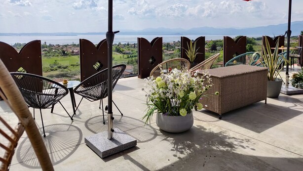 A terrace with outdoor seating, red umbrellas, and a view of the landscape. - Hotel Castello S. Antonio (Lazise)