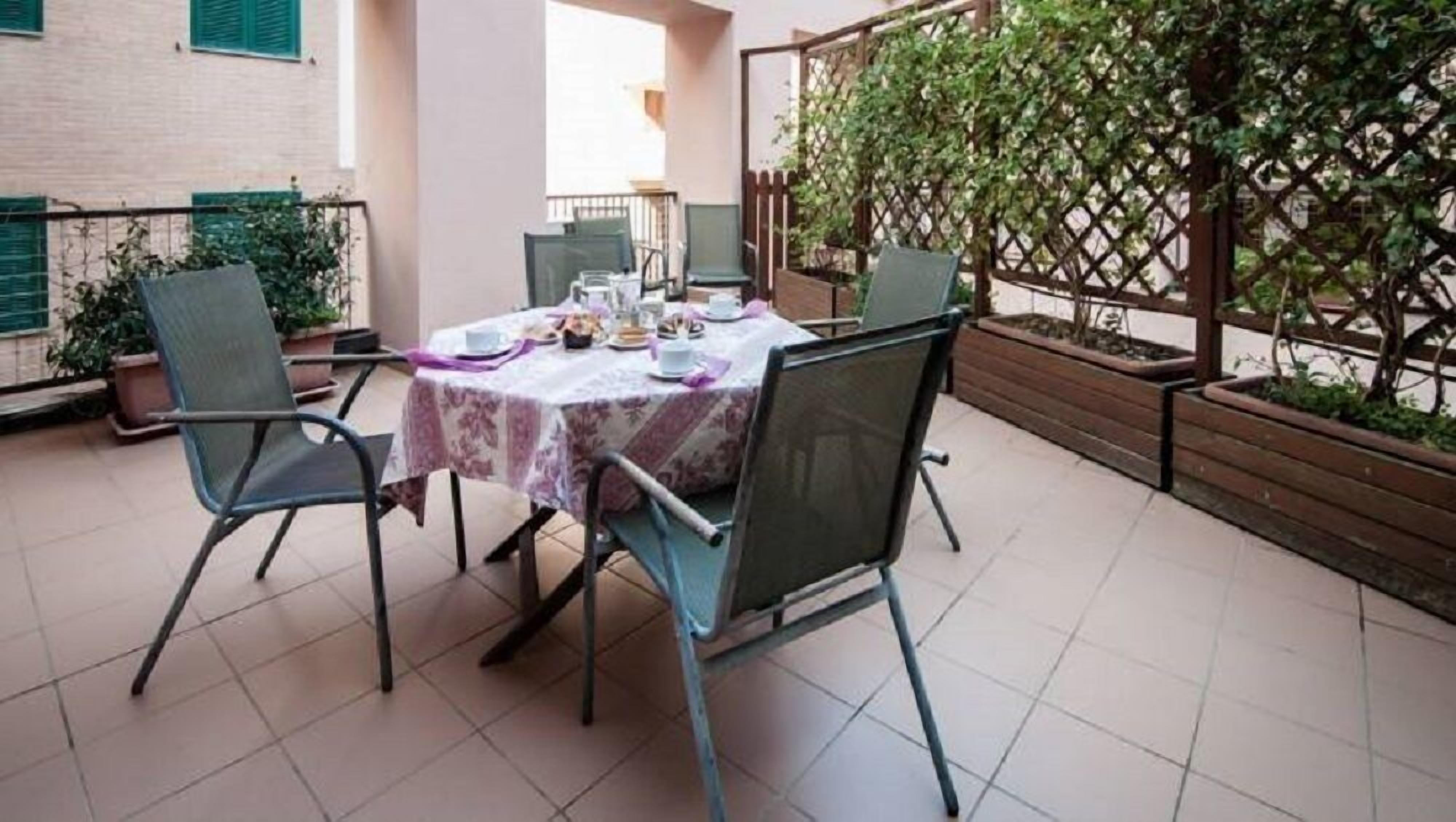 A patio with a table set for four, surrounded by chairs, and a wooden trellis with climbing plants.