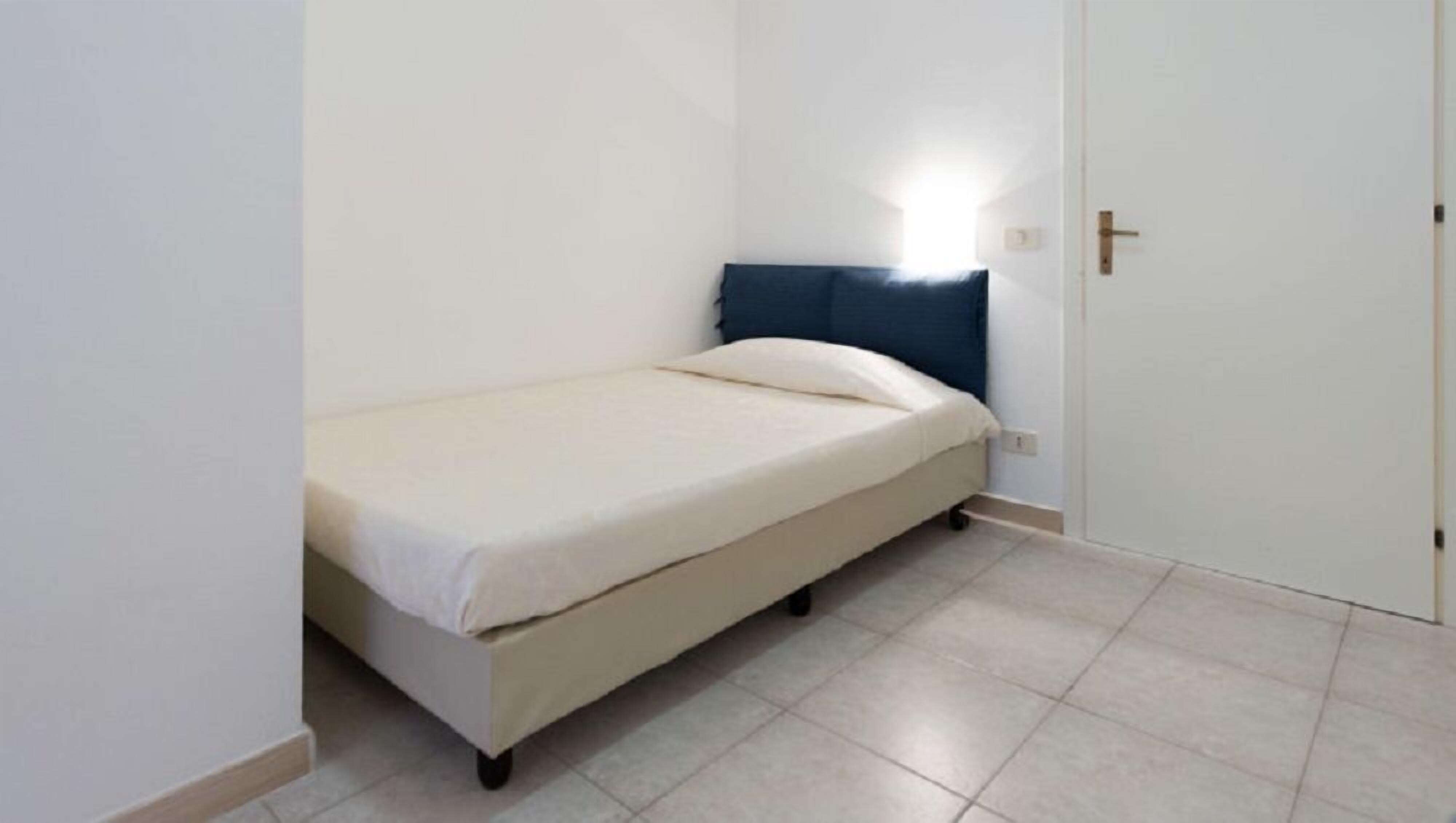 A small, single-bed room with a white wall and a door.