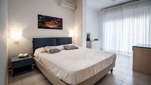 Une chambre bien rangée, avec un lit, des tables de chevet, une petite commode et un petit bureau, ainsi qu’une plante en pot.