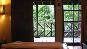 A room with a bed, a wooden door, and a view of a balcony with greenery. - The Last Frontier Boutique Resort			 (Kota Kinabatangan)