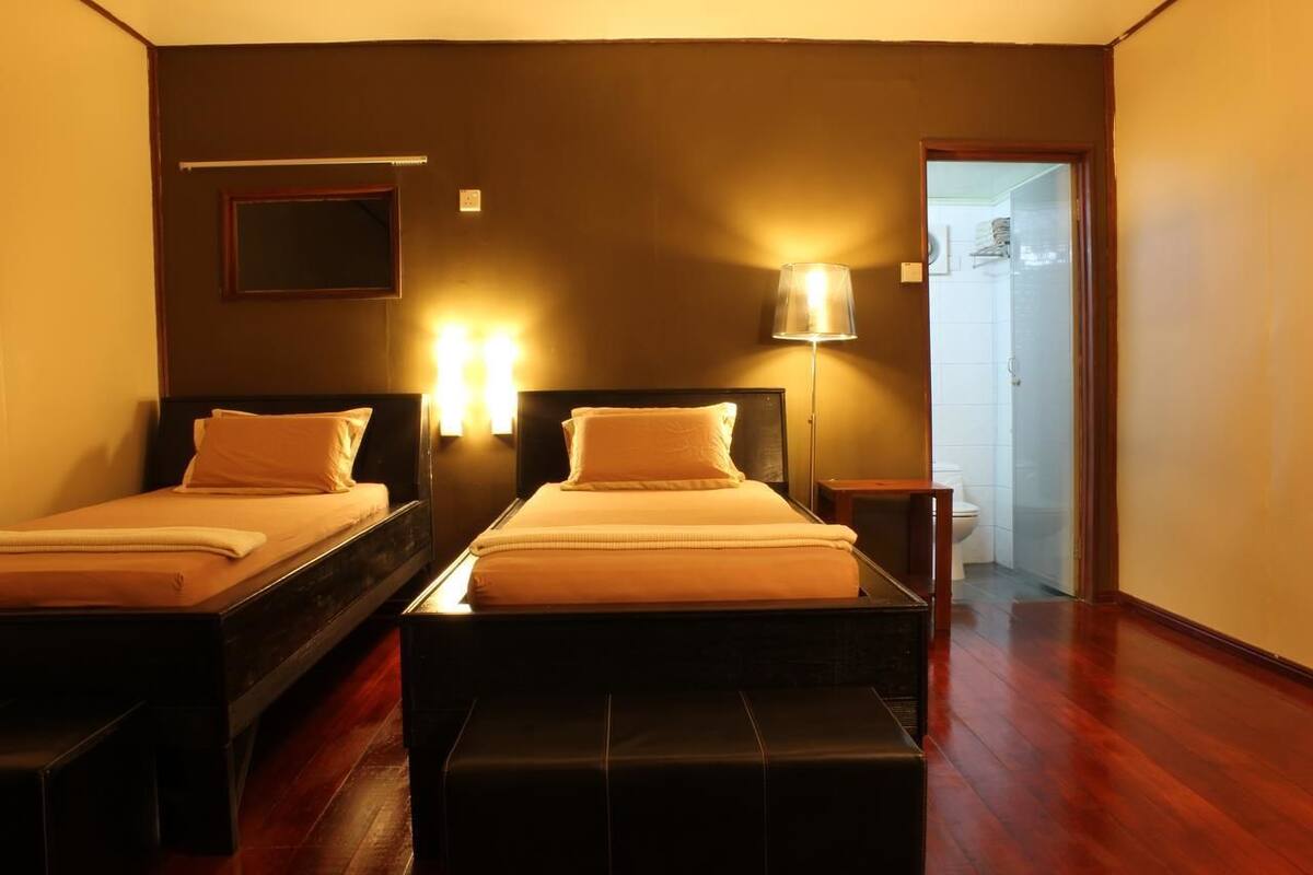 Una habitación de hotel con dos camas, una mesita de noche, una lámpara y una puerta que da a un baño.