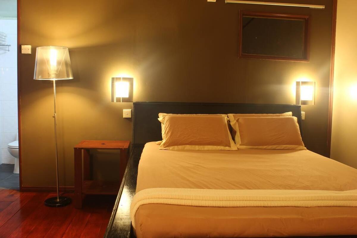 Una cama bien hecha con dos almohadas, una mesita de noche con una lámpara y dos luces empotradas en la pared.