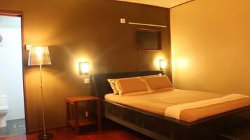 A hotel room with a bed, bedside table, lamp, and wall-mounted light fixture.