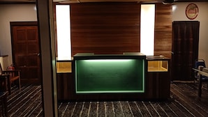 A reception area with a wooden reception desk, a green illuminated panel, a ceiling fan, and a wooden door. - The Last Frontier Boutique Resort			 (Kota Kinabatangan)