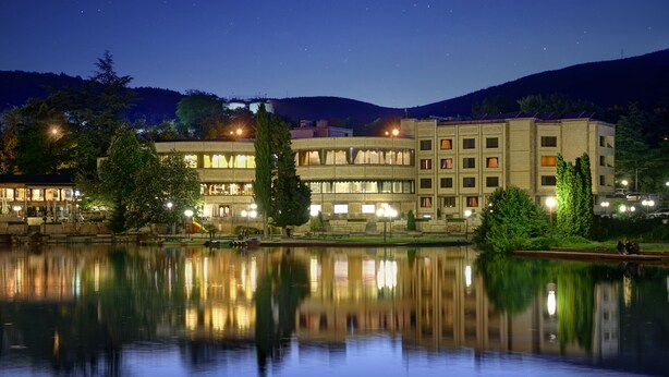 Un hotel de varios pisos, reflejado en el agua, con una montaña al fondo.