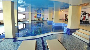 An indoor swimming pool with clear glass walls, lounge chairs, and exercise equipment. - Park Hotel Stara Zagora (Stara Zagora)