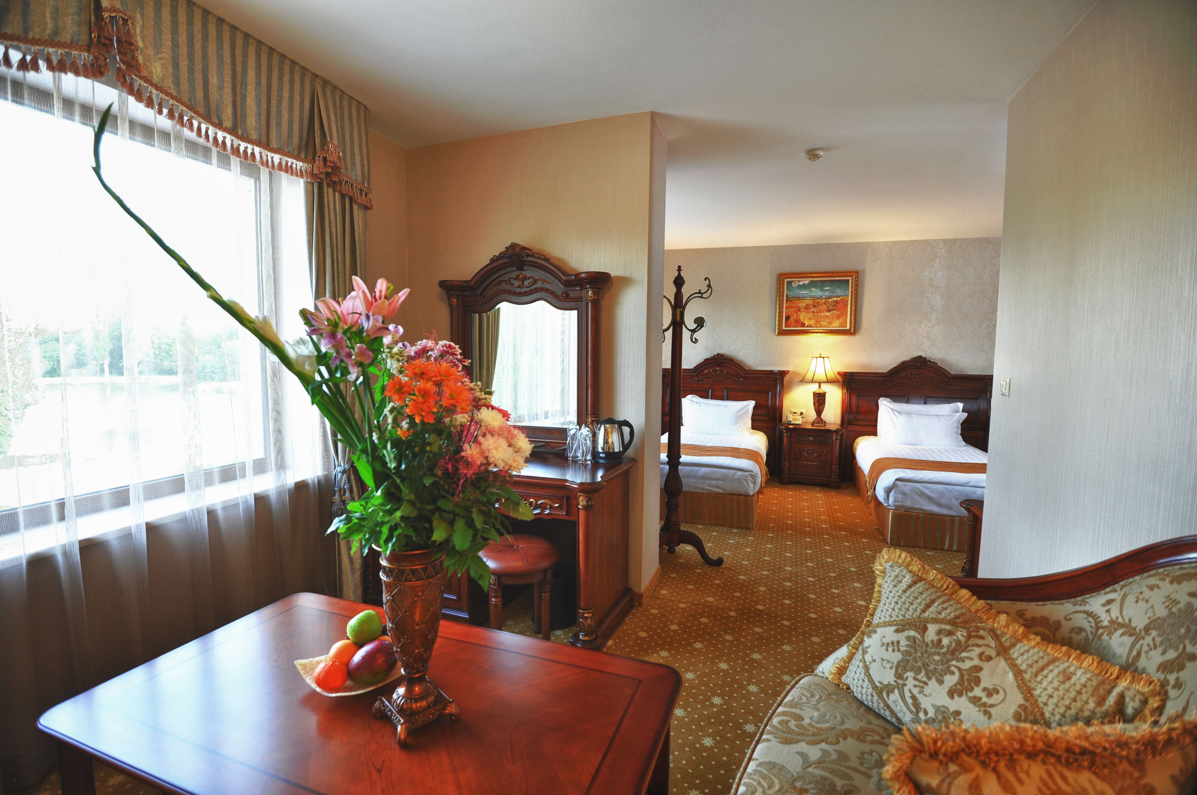 Habitación de hotel con un escritorio de madera, un florero, una cama con dos almohadas, una mesita de noche con una lámpara y un cuadro en la pared.