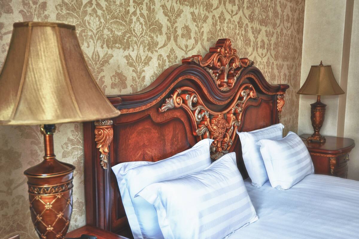 Un lit avec une tête de lit décorée, deux lampes de chevet et un papier peint à motifs floraux.