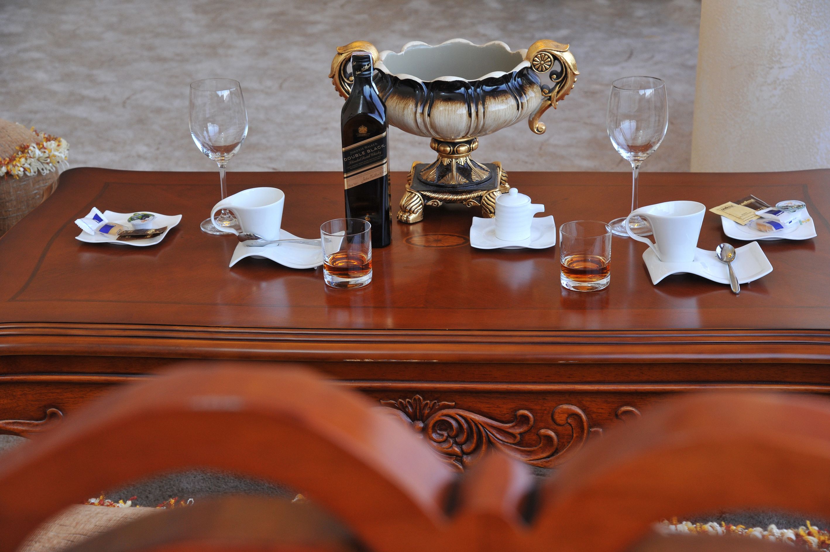 A wooden table with a decorative bowl, two wine glasses, and a bottle of wine.