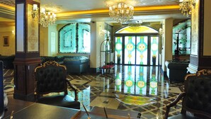 Un lobby imponente con candelabros ornamentales, un amplio ventanal de vitral y una zona de estar lujosa.