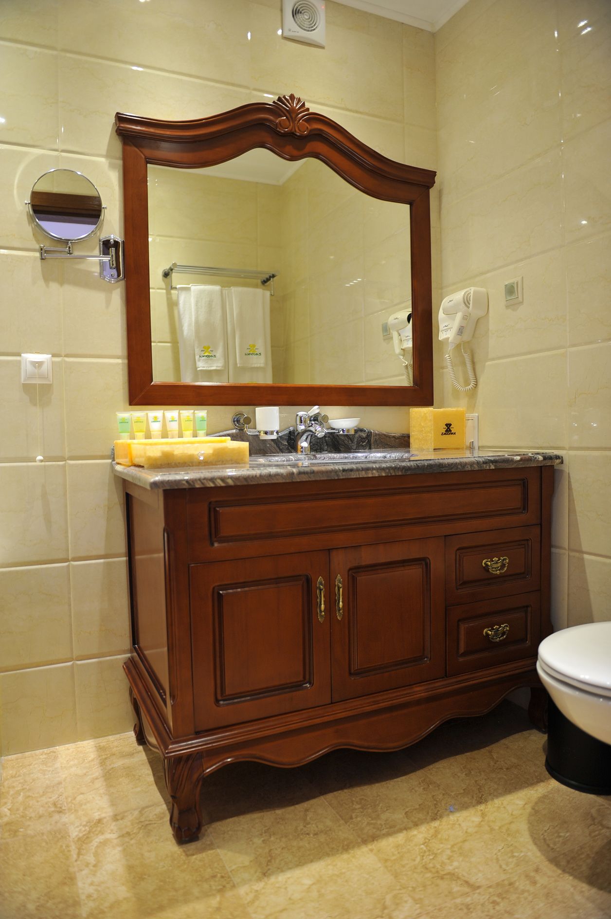 A bathroom with a wooden vanity, a large mirror, a hairdryer, and a toilet.
