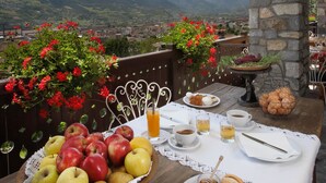 Una mesa dispuesta con frutas, pan, queso y bebidas, con vistas a un paisaje montañoso.