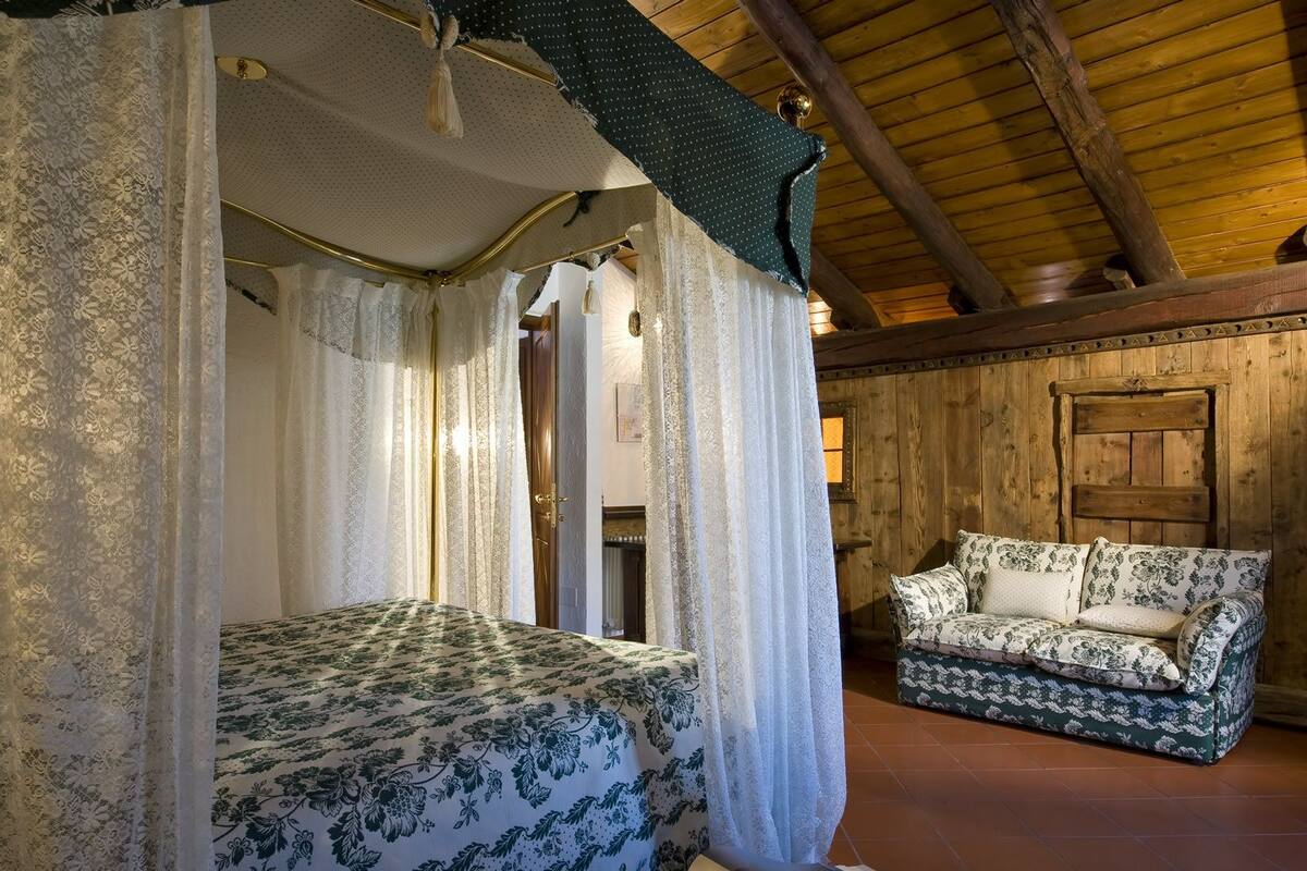 A bedroom with a canopy bed, a wooden ceiling, and a floral-patterned sofa.
