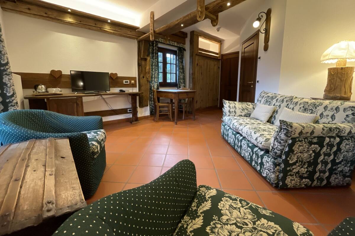 A cozy living room with a sofa, a wooden table, a TV, and a dining area with a window.
