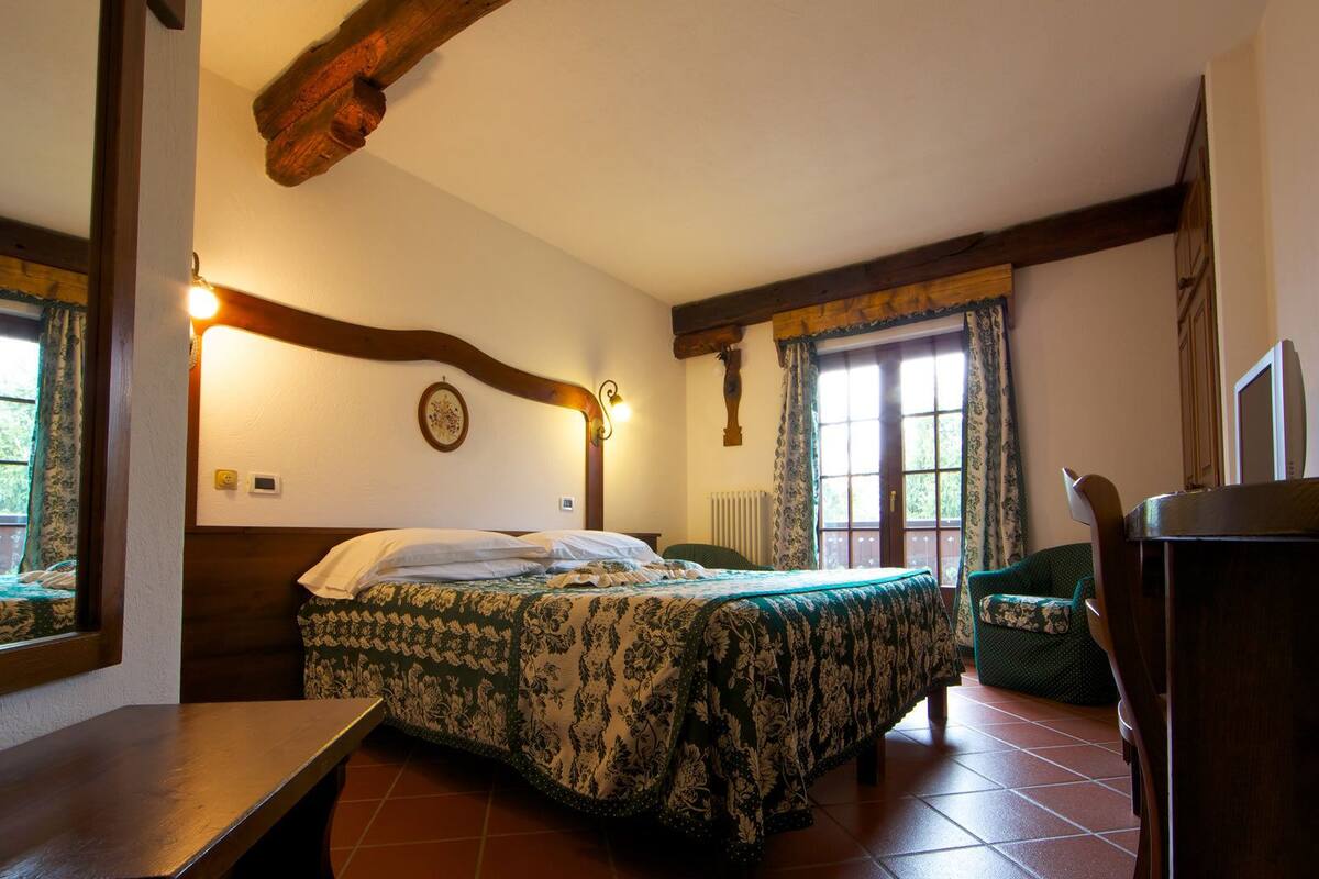 A bedroom with a bed, a chair, a desk, and a window with curtains.