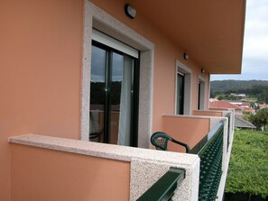 A balcony with a green chair, a window with a white frame, and a view of a town with red-roofed buildings. - Hotel Cachada (Sanxenxo)
