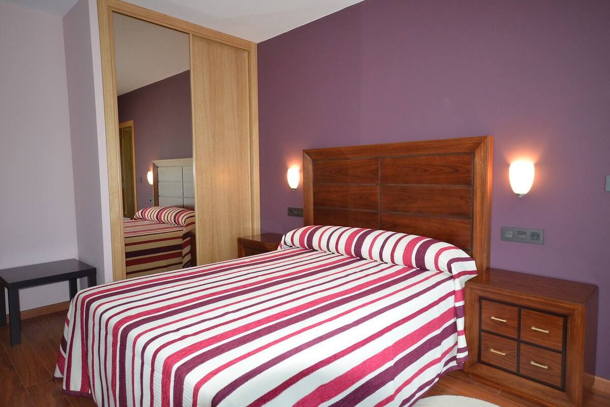 A bedroom with a bed, wooden headboard, bedside tables, and a mirror.