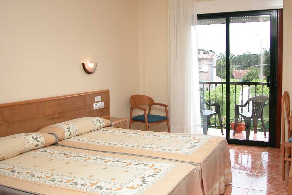 A hotel room with a bed, a chair, a table, and a balcony with chairs.