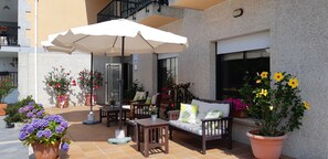 An outdoor patio area with a wooden sofa, a table, and an umbrella. There are potted plants and flowers around. - Hotel Cachada (Sanxenxo)