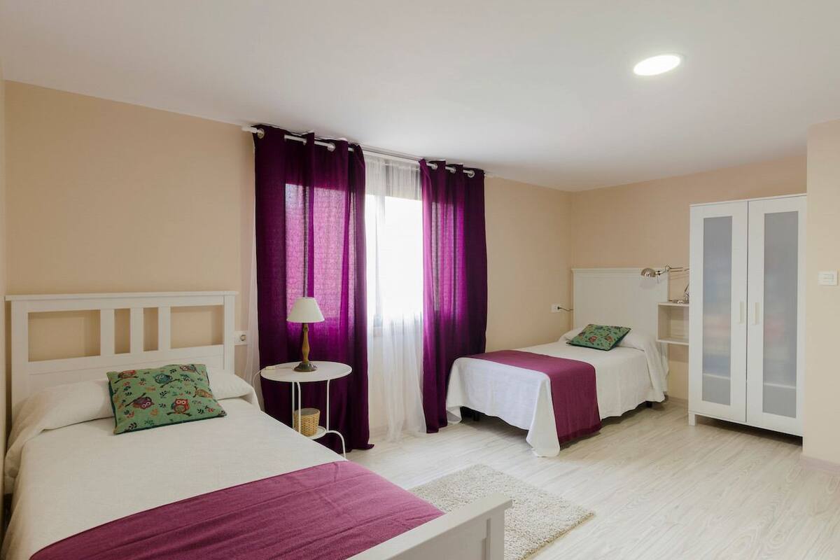 A bedroom with two beds, a nightstand, a lamp, and a wardrobe.