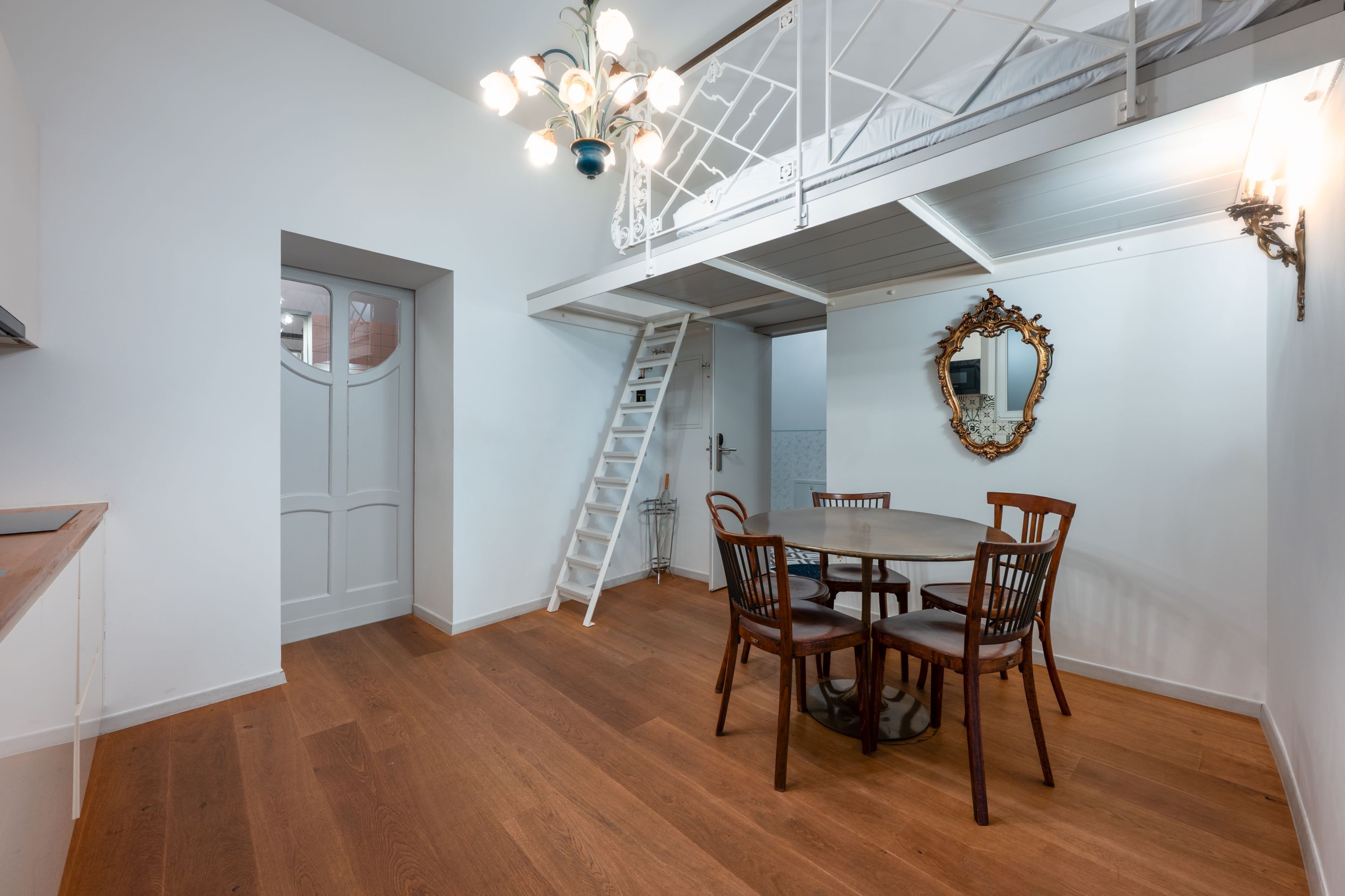 A dining area with a round table, wooden chairs, a chandelier, a ladder, and a door.