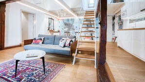 A modern living room with a sofa, coffee table, and patterned rug. A staircase leads to an upper level.