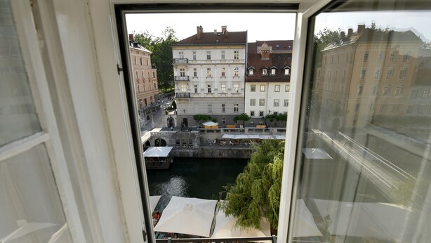 A view from a window overlooking a riverside square with buildings, a bridge, and outdoor seating areas.