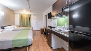 Una habitación de hotel compacta con dos camas, kitchenette, televisor y ba ño.