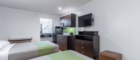 A hotel room with two beds, a kitchenette, a TV, and a dining area.